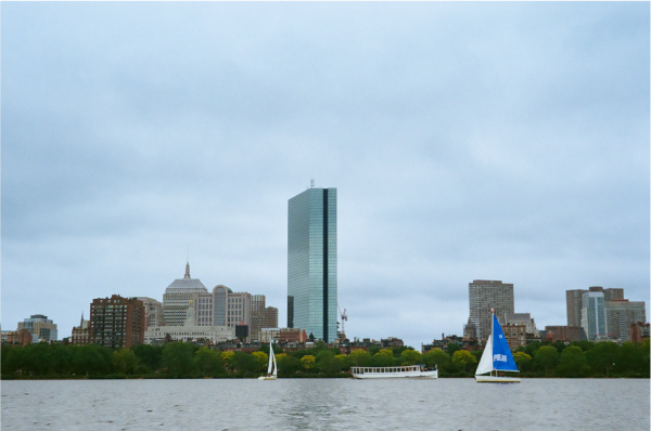 Boston skyline from the Charles River, set against an overcast grey sky.