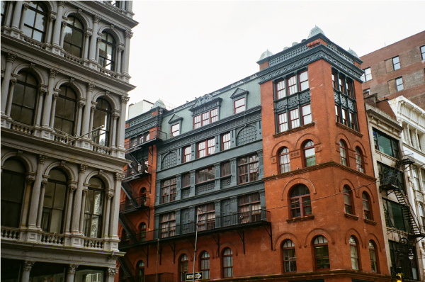 A large copper and red-bricked building at an intersection, against an overcast grey sky.
