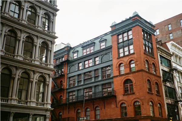 A large copper, and red-bricked building at an intersection, against an overcast grey sky.