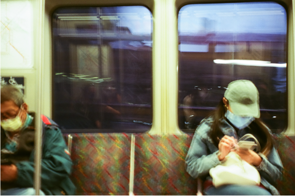 Blurry shot of two rapid transit passengers looking down at phone while sitting down on the train.