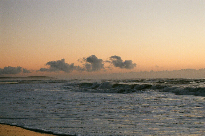 The waves crashing onto a beach at sunset.